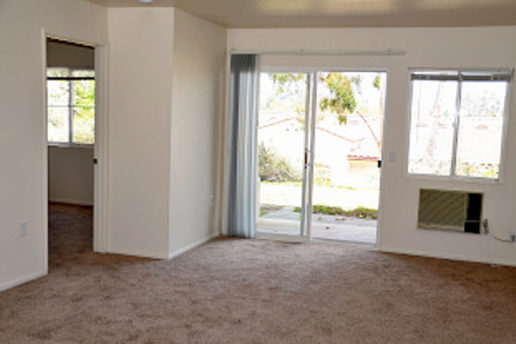carpeted living room facing patio with sliding glass doors, window, build-in wall AC, and bedroom door