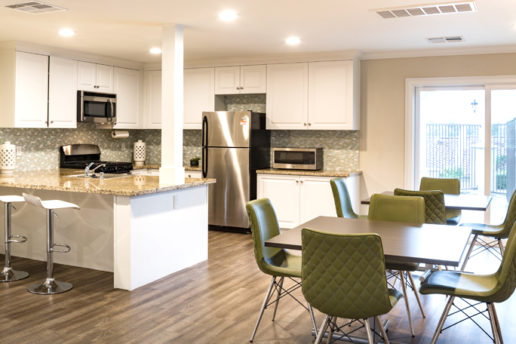 Large kitchen with granite countertops, white cabinets, gray hardwood floor, dining area with tables and green chairs