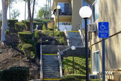 exterior of staircase up hill with trees and shrubs, sidewalk with outdoor lighting leading to parking area with handicap parking sign