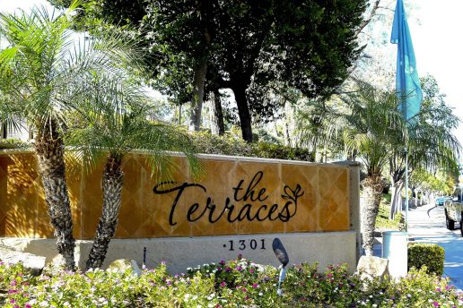 Tiled brown The Terraces sign with 1301 number surrounded by palm trees and plants